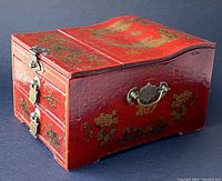 View of the jewelry box closed showing red lacquer finish with gold dragon and floral designs and metal side handle