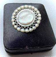 Close-up of the round vintage mother of pearl brooch with iridescent center on top of a closed black presentation case.