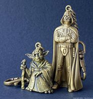 Front view of Yoda and Darth Vader brass-tone metal keychains together.