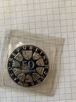 Front side of the 50 Shillings silver coin sealed in plastic, showing denomination and multiple coats of arms.