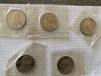 Five sealed USSR 5 ruble coins placed on graph paper, each in a separate plastic protective sleeve, showing various sides and designs including workers, emblems, and historical figures.