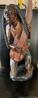Front view of the wood carving showing detailed facial features, dreadlocks, guitar, and seated pose.