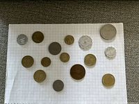 Collection of 17 Israel coins of various sizes, metals, and shapes laid out on grid paper