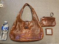 Brown croc-embossed leather women's handbag with matching small pouch and mirror beside it and water bottle for scale