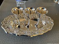 Three silver plated goblets placed on a decorative silver plated tray with floral and scroll patterns, shows full view of tray and goblets for condition and design assessment.