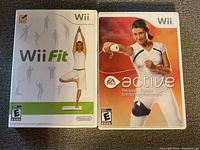 Two Nintendo Wii fitness games side by side with visible front covers: Wii Fit and EA Sports Active Personal Trainer.