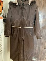 Front view of brown winter puffer coat with fur trimmed hood and geometric stitched design on arms and chest area