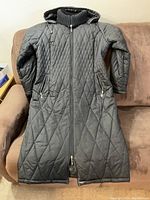 Front view of black quilted winter coat with long length, hood, and front zipper.