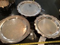 Three silver-plated serving trays, one round with ornate beaded floral edge, two oval with scalloped edges