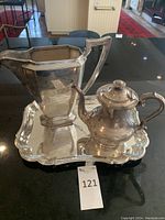 Set of three silver-plated pieces including tray, pitcher, and teapot displayed on a black surface.