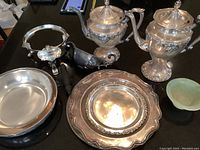 Overview of assortment of sterling plate items and small green bowl on black surface