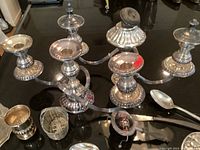 Two silver plated three-arm candelabras on counter alongside other pieces