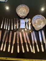 Overview of two shell dishes, line of butter spreaders/bread knives, picks, and spoons