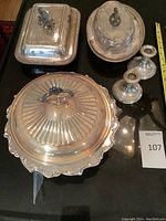 Full view of all items including three silver plated serving bowls with lids and two small sterling silver candlesticks, one dented.