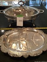 Photo of silver plated serving dish with lid, ornate handle, and feet, shown with measuring tape and auction tag.