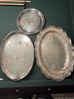 Four silver plate platters displayed on a dark surface showing shape variety and tarnish
