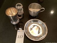 Four silver-plated items: two mugs, one bowl, and one engraved cup shown on black surface.