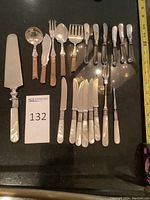Full view of all silver plated and mother of pearl handled utensils laid out on black surface for display.