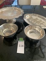 Overview of all silver plated serving pieces on black surface including pedestal tray, meat carving dish, and two bowls.