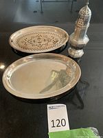 Two oval silver plated trays (one plain, one pierced) and a silver plated spice shaker on black countertop
