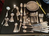 All flatware pieces and pierced platter laid out on black surface