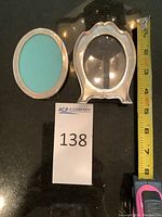 Two oval photo frames placed next to each other, showing size with tape measure. One frame is Tiffany silver, the other silver plated.