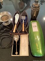 Lot showing electric burner, silver plated bar shaker, Wallace silver plated dish with emerald green surface, silver plated utensils with cream handles in leather case, and boxed silver plated spoon.