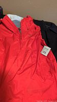 Red Patagonia shell jacket with hood and zip front displayed on surface alongside black trench coat.