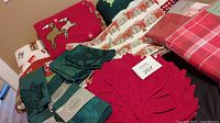 Photo showing assorted Christmas linens including red felt maple leaf placemats, green cloth napkins, fleece throws with holiday prints, and woven placemats.