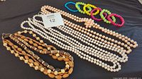 All items laid out including 4-strand wooden necklace, two 60-inch pearl strands, one 64-inch peach pearl strand with knots, and six assorted bracelets.