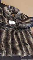 Full view of the ladies medium faux fur plush coat with belt laid out showing texture and color shades.
