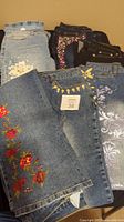 Six pairs of embellished Diane Gilman jeans showcasing beaded, sequin, rhinestone, and embroidered floral designs in various denim washes.