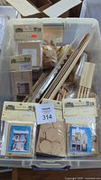 Plastic container filled with multiple miniature laser cut homemade dollhouse kits, wooden trims, sticks and spindles for stairs, shingles and other building components.