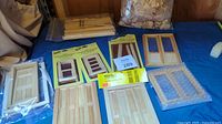 Photo of multiple wooden dollhouse windows, doors, and packaged wooden pieces including shakes and trim.