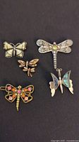 Five insect-style brooches and barrette arranged on black background showing intricate details and stone accents