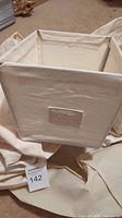 Beige fabric storage bin with label slot on front, shown against fabric background.
