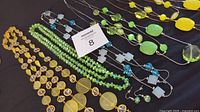 Overview of faceted and beaded necklaces in various colors including yellow, green (peridot), and blue with matching earrings visible.