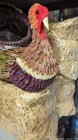 Front and side views of a turkey figurine crafted from natural materials like straw and corn husks placed on hay bales.