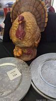 Resin turkey statue with autumn accents, positioned behind two silver-tone charger plates with textured decorative patterns.