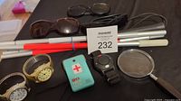 Overview photo showing all items including watches, emergency alert devices, cane, glasses, and magnifying glass arranged together on a surface.