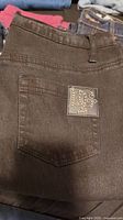 Black Diane Gilman jeans folded showing back pocket with studded DG logo patch.