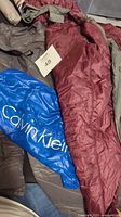 Grey Calvin Klein down jacket with blue branded packable bag and burgundy ExOfficio jacket beneath it