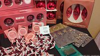 Photo showing assorted boxed Martha Stewart glass ornaments in red, including teardrop and round shapes, beaded garlands, and ornament hooks on a black surface.