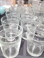 Photo showing a group of clear glass tumblers with ribbed textured upper portions, stacked on a table