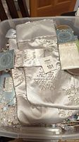 White satin stockings with embroidered snowflakes and bead trim in a plastic bin shown with tags and ribbons.