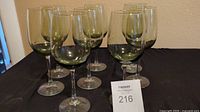 Photo showing six stemmed wine glasses with green tinted bowls against a black cloth background.