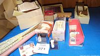 Overview photo showing miniature furniture pieces, boxed bathroom suite items, and wallpaper rolls arranged on a blue table.