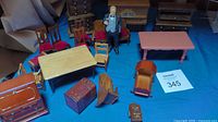 Overview photo showing multiple miniature wooden furniture pieces including tables, chairs, a chest, and a standing figurine of a man
