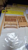 Miniature wooden furniture cabinets and display pieces on table with boxed flooring and ceiling tile kits behind them.