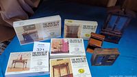 Photo shows five boxed kits from The House of Miniatures and three miniature wooden furniture pieces displayed on a surface.